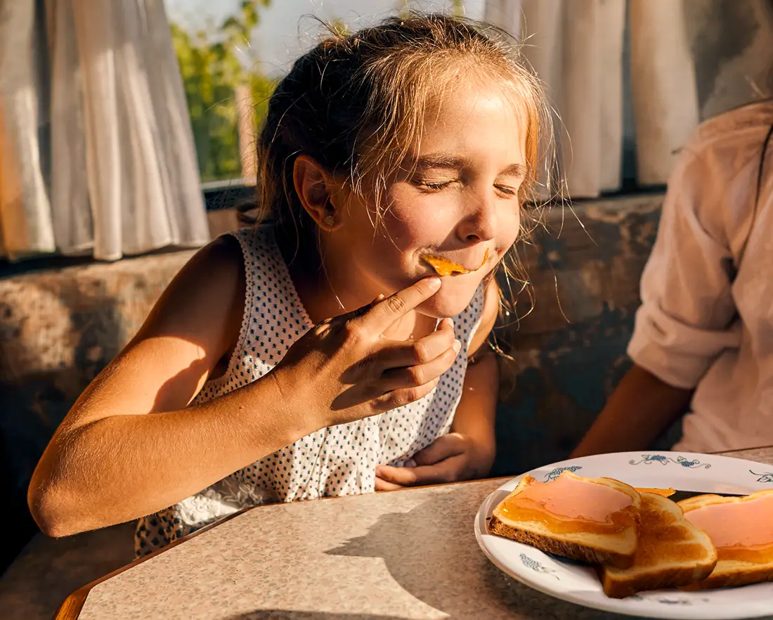 Ein Mädchen beißt herzhaft in ein Brot mit Langnese Honig.
