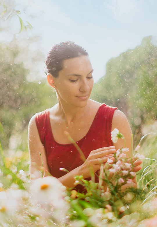 Frau sitzt in einer Blumenwiese und schaut sich die Blumen an.